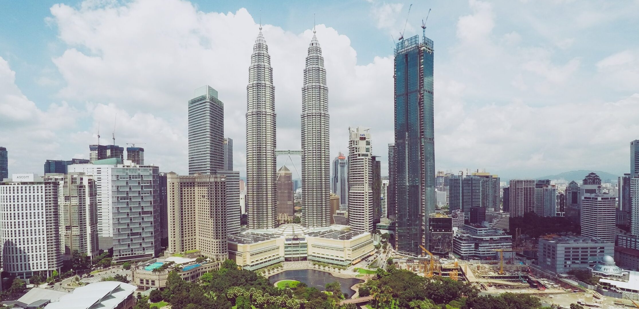 An aerial shot of Petronas Twin Towers near skyscrapers and trees under a blue sky in Kuala Lumpur, Malaysia